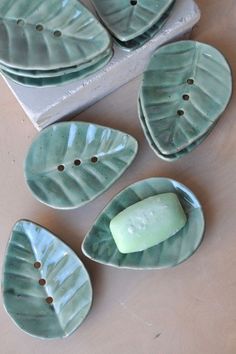 four green leaf shaped dishes sitting on top of a white table next to a block of soap