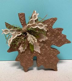 a metal object with leaves and flowers on it's side against a blue wall