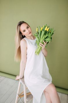 a woman sitting on a stool holding a bunch of flowers