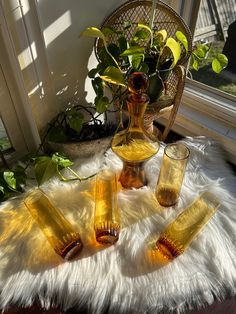 four yellow glass vases sitting on top of a white fur covered floor next to a potted plant