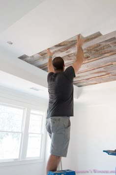 a man standing on top of a ladder working on a wood plank ceiling in a room