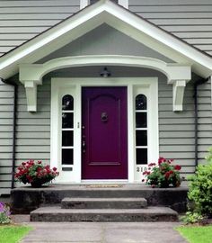 a purple door sits in front of a gray house with white trim and flowers on the steps