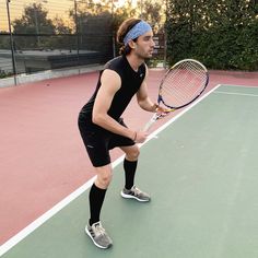 a man holding a tennis racquet on top of a tennis court in front of a fence