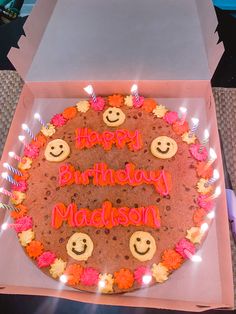 a happy birthday cake with candles and smiley faces on it, sitting in a box