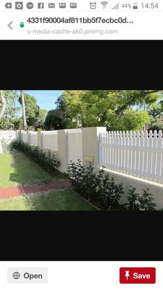 a white picket fence in front of a house with trees and bushes on the other side