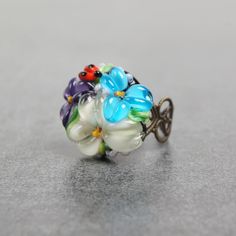 This romantic Glass ladybug flower ring is a perfect gift for women. It's very tender and unique! Set Matching bracelet: https://www.etsy.com/listing/161559547 Matching earrings: https://www.etsy.com/listing/200833152 Matching pendant: https://www.etsy.com/listing/161556072 Dimensions: the ring is adjustable. The bead is 2.2-2.4cm in diameter. Materials: artist lampwork bead, metal fittings. Colors used: blue, white, lilac, violet, green. Please, note, each bead is made by hand and may differ sl Dainty Jewelry With Handmade Flowers For Gift, Dainty Jewelry With Handmade Flowers As Gift, Whimsical Adjustable Ring, Whimsical Adjustable Jewelry Ring, Adjustable Whimsical Ring, Delicate Flower Ring As Gift, Whimsical Flower Shaped Jewelry For Gift, Whimsical Flower Shaped Jewelry As Gift, Whimsical Flower Shaped Jewelry Gift