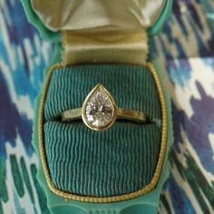 a ring with a pear shaped diamond sits in a green box on a patterned surface