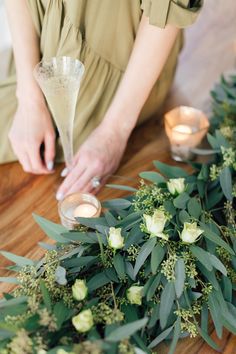 a woman sitting at a table with candles and flowers on the floor next to her