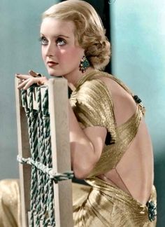 a woman in a gold dress leaning against a fence