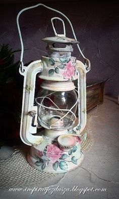 an old fashioned oil lamp with flowers painted on it's side and the light is turned on