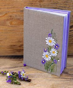 a book with daisies and purple flowers on the cover sitting on a wooden table