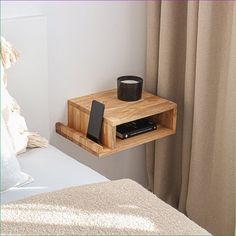 a wooden shelf holding a cell phone and a cup on it next to a bed