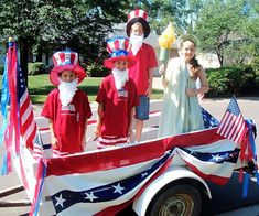 children in patriotic outfits are riding on an old fashioned truck with flags and santa clause hats