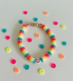 a bracelet with multicolored beads and a smiley face charm is on a white surface surrounded by confetti