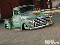 an old green truck parked in front of a red brick building with graffiti on it's side