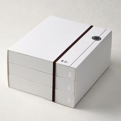 a white box with a brown ribbon around the top and sides on a gray surface