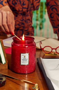 a person lighting a candle on top of a wooden table next to books and glasses