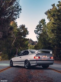 a silver car parked on the side of a road next to some trees and bushes