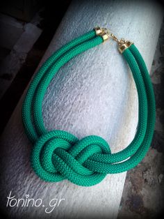 a green rope bracelet with gold clasps on a white piece of wood next to a brick wall