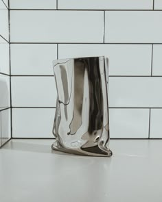 a silver vase sitting on top of a counter next to a white tile backsplash