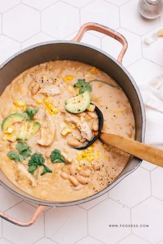 a large pot filled with food on top of a white countertop next to a wooden spoon