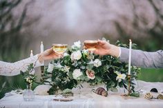 two people toasting glasses over a table with flowers and greenery on the table