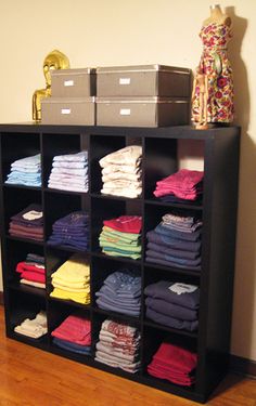 a black shelf filled with lots of different colored shirts on top of wooden flooring