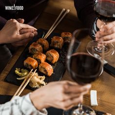 two people are eating sushi with chopsticks next to a glass of wine