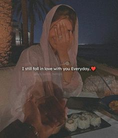 a woman covering her face while sitting at a table with food and drinks in front of her