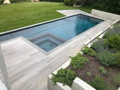 an outdoor swimming pool surrounded by greenery and wooden decking, in the middle of a lush green yard