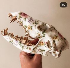 a hand holding an animal skull with flowers on it's back and teeth missing