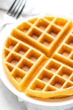 a waffle on a white plate with a fork and knife in the back ground