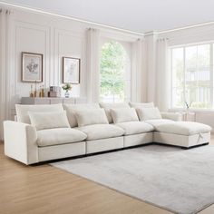 a living room with white furniture and large windows in the backround, along with an area rug on the floor