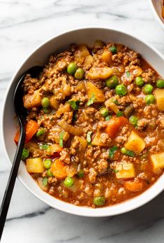 a bowl filled with meat and vegetables on top of a white table next to a spoon