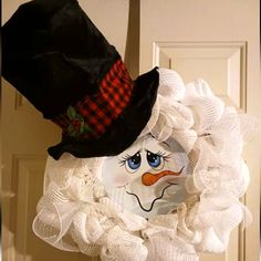 a white wreath with a black hat and snowman's face painted on it