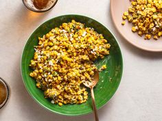 a green bowl filled with corn next to two plates