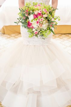 a woman in a white dress holding a bouquet of flowers on top of a bed