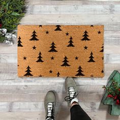 a person standing in front of a door mat with christmas trees on it