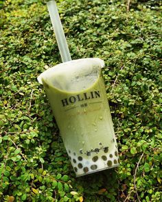 a plastic cup with a straw sticking out of it sitting on top of green plants