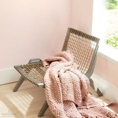 a chair with a pink blanket on it next to a window in a room that is painted pink