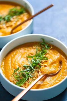 two white bowls filled with carrot soup and garnished with parsley