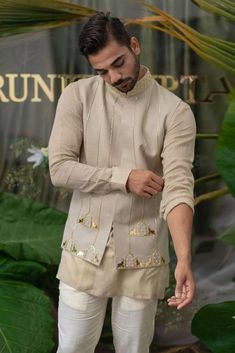 a man standing in front of a green plant wearing a white outfit with gold accents