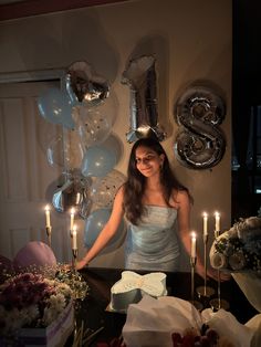 a woman standing in front of a cake with candles on it and balloons behind her