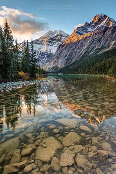 a mountain lake surrounded by trees and rocks in the foreground, with snow capped mountains in the background