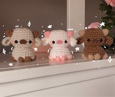 three small crocheted animals sitting on top of a white mantle next to pink flowers