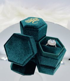 three green velvet jewelry boxes sitting on top of a white plate with a diamond ring in it