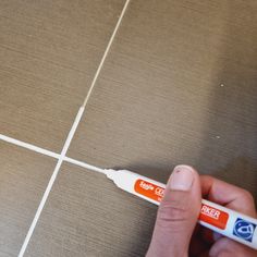 a person is holding an orange and white toothbrush in their left hand on a tile floor