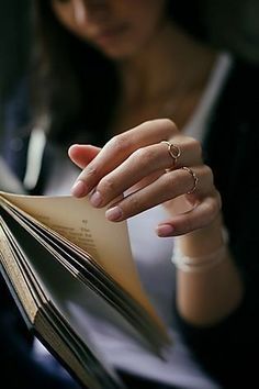 a woman is holding an open book and looking at it with her hand on the pages