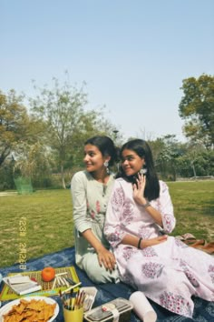 two women sitting on a blanket in the grass