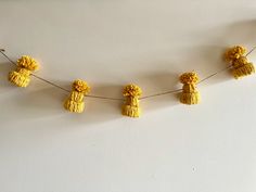 small yellow pom poms are hanging from a string on a white wall,